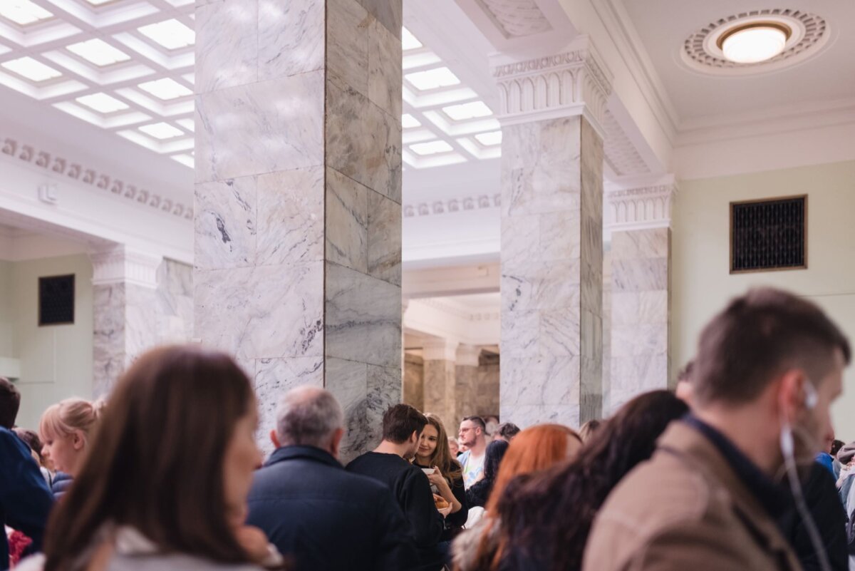 Crowd of people in the Palace of Culture and Science and among them a girl leaning against one of the columns