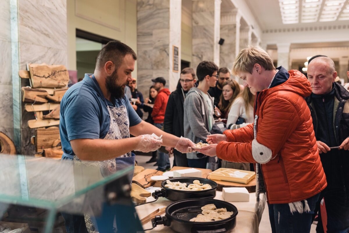 Man hands dumpling to woman in red jacket