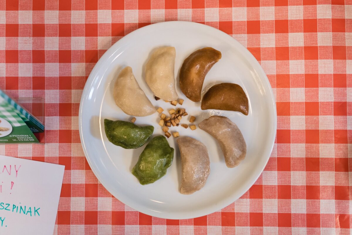 Nicely arranged dumplings in different colors on a white plate standing on a red and white checkered tablecloth