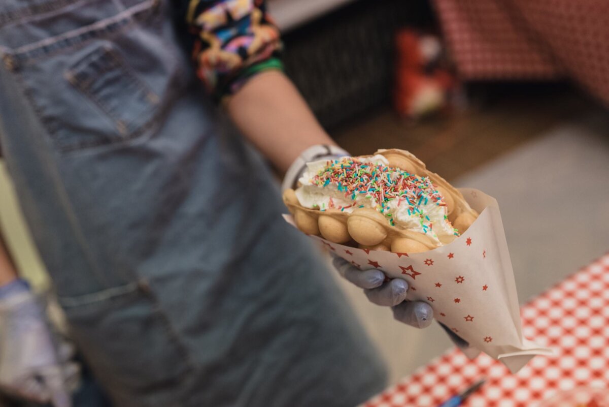 A hand holding a waffle with whipped cream and colored sprinkles