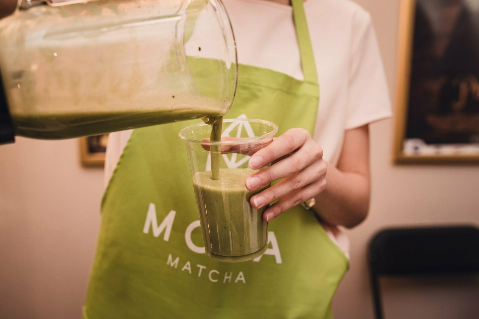 Woman pours green shake from pitcher into glass