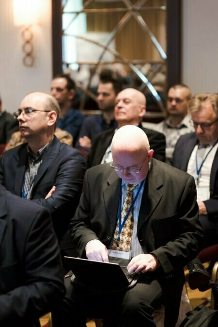 Man with glasses in audience does something on laptop