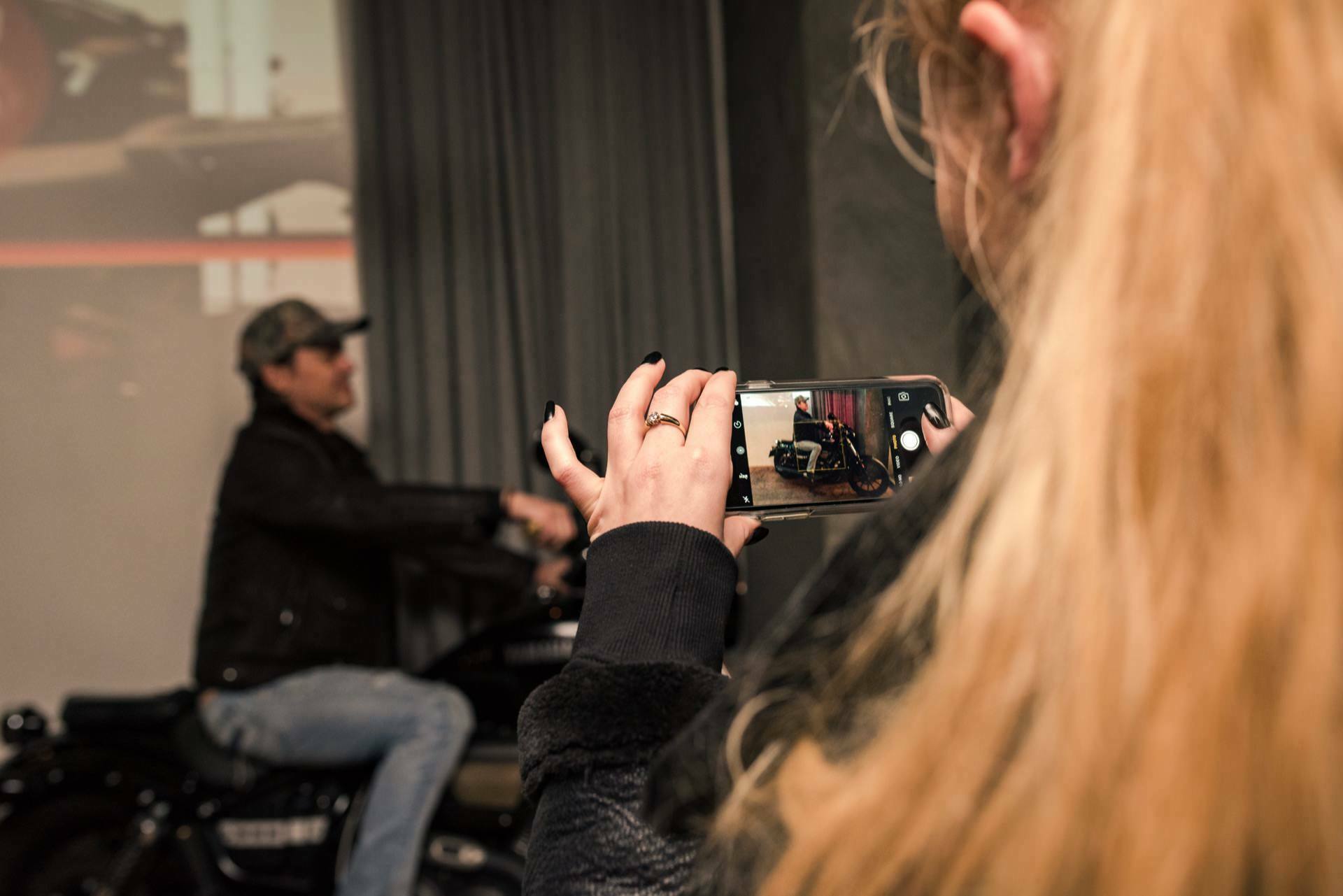 Woman takes phone photo of man sitting on motorcycle