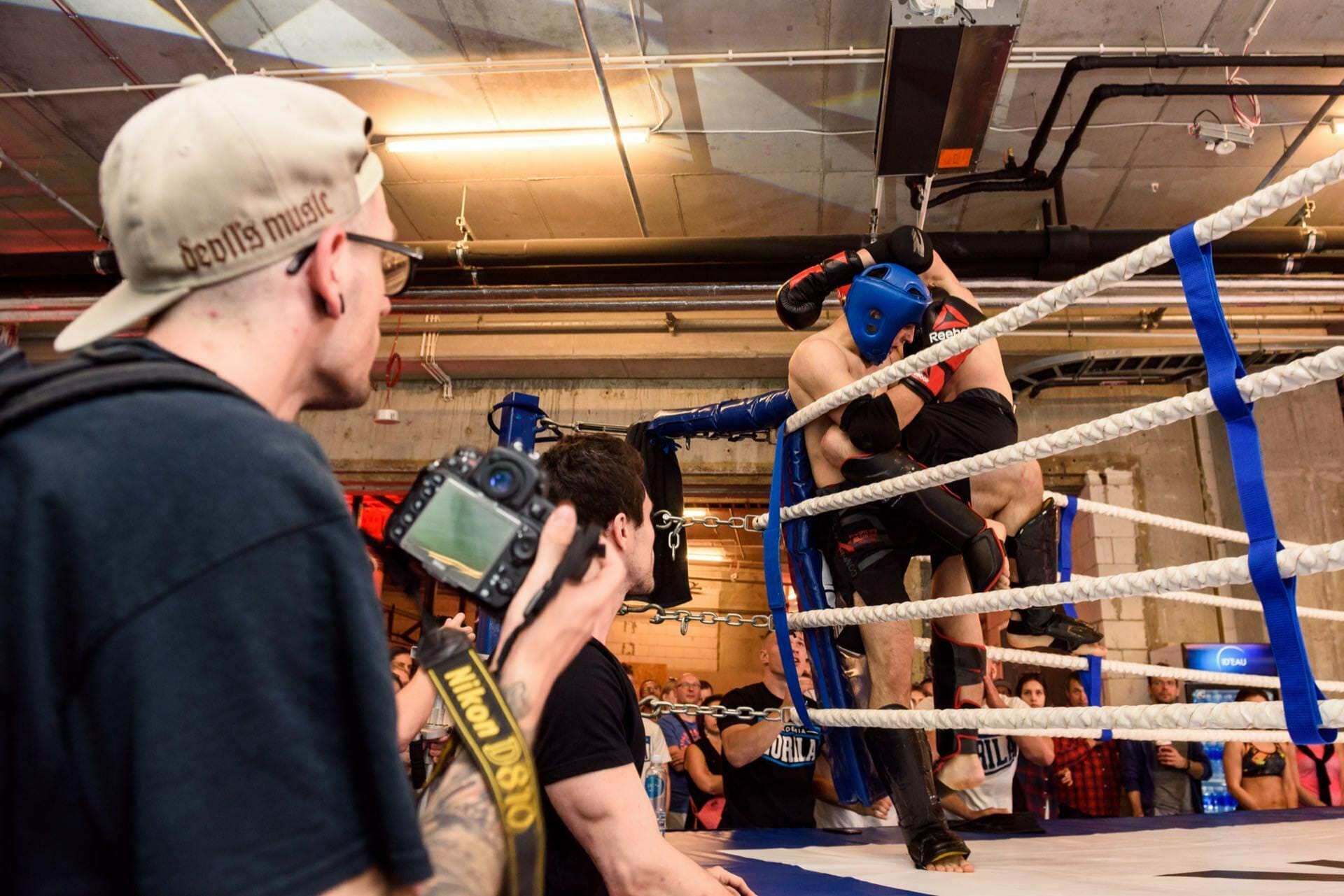 A photographer wearing a hat tries to capture the fight of the competitors in the corner of the ring