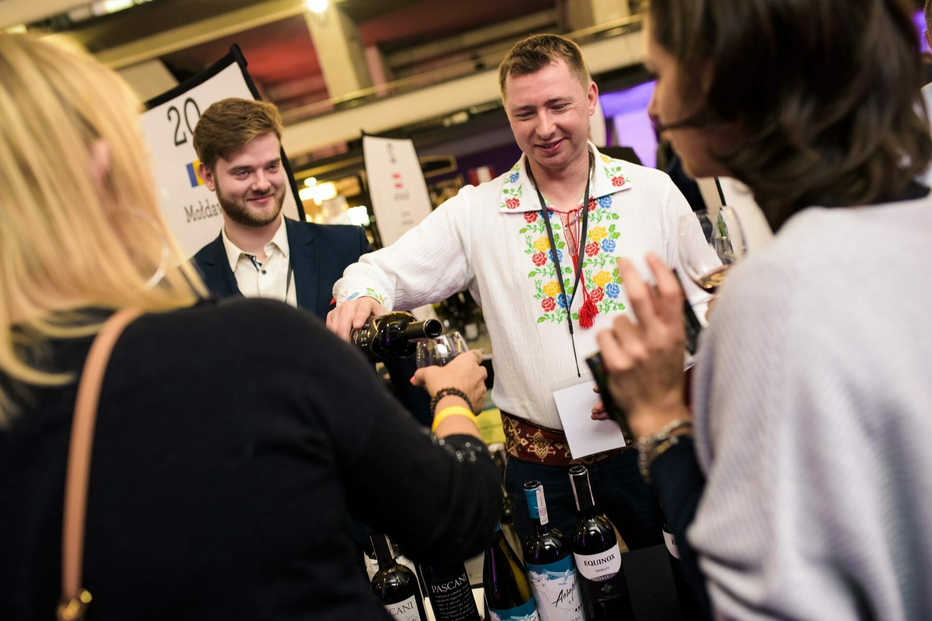 A man in a floral shirt pours wine into a woman's glass