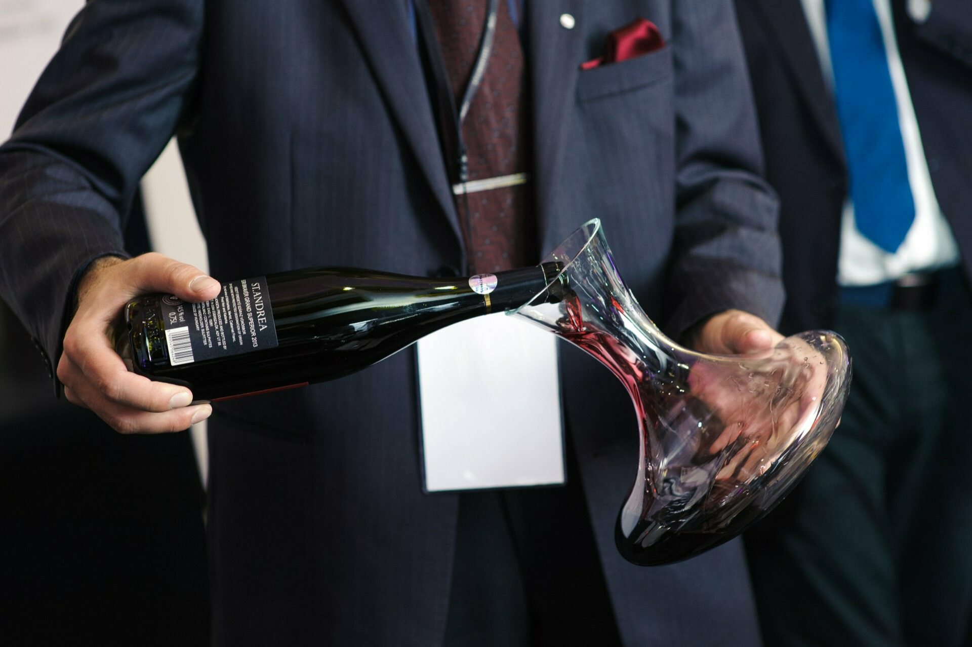 A man pours wine from a bottle into a glass vessel