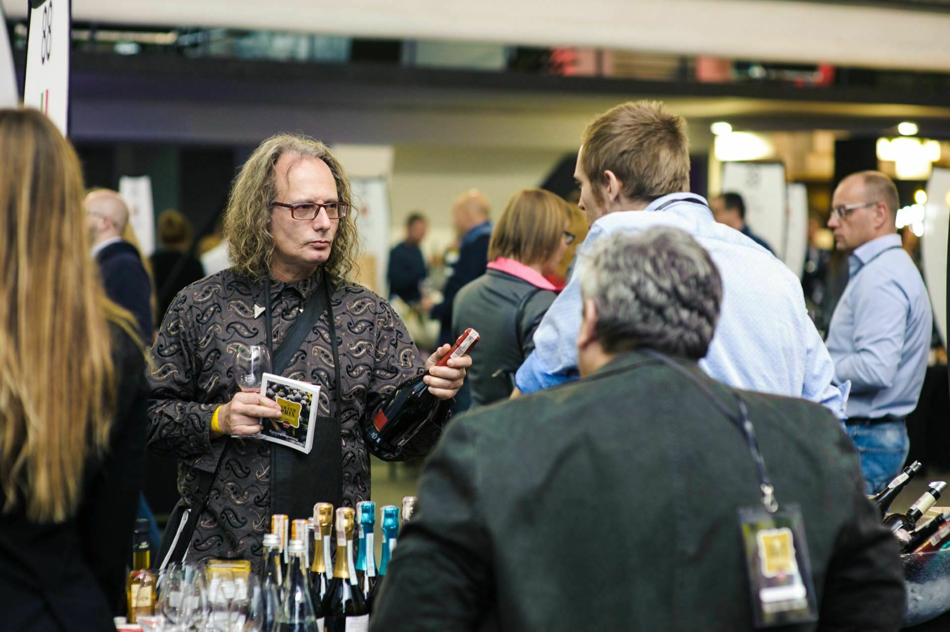 Man with long hair holds bottle and wine glass