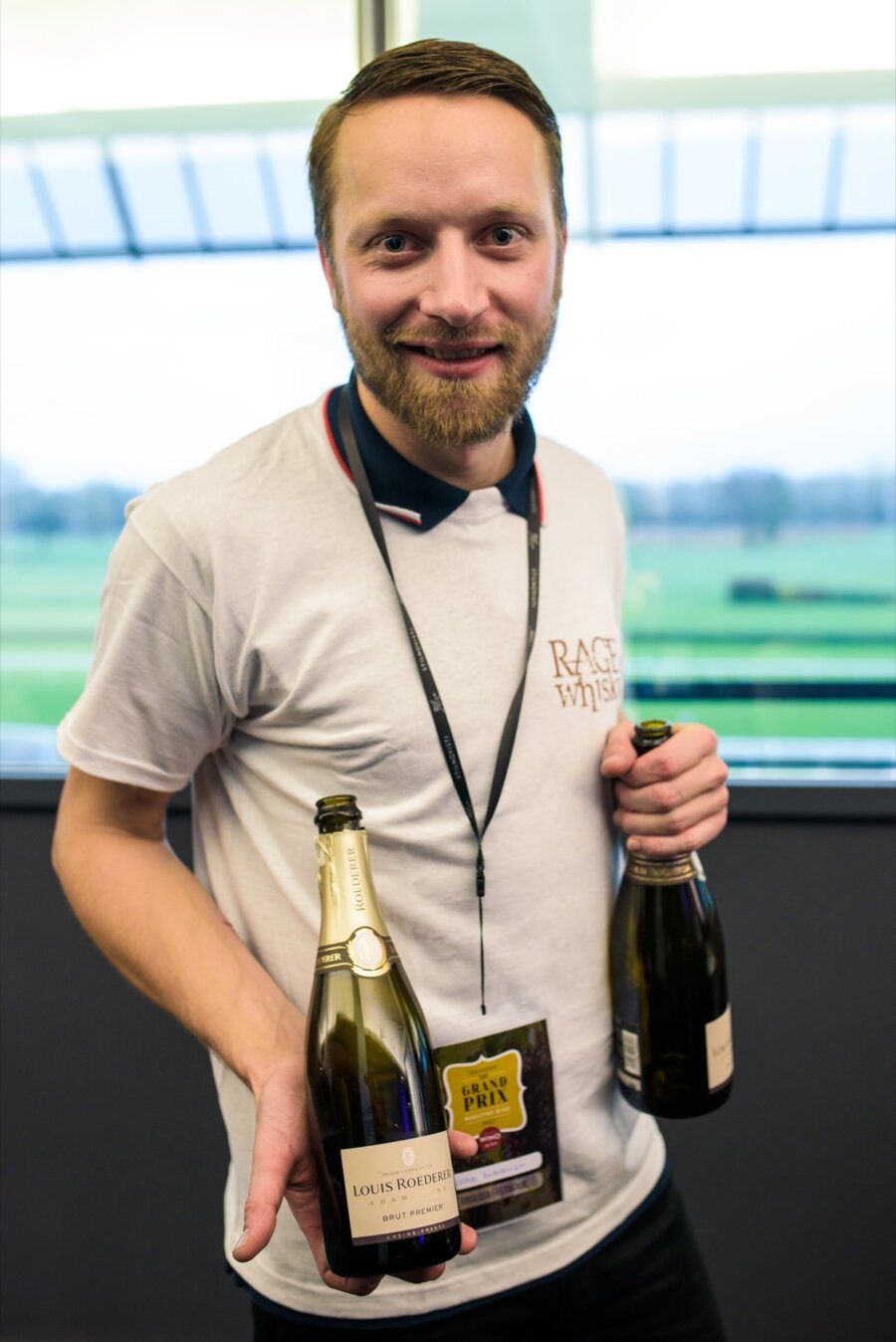 Man with beard at Służewiec horse racing track holds bottles of wine