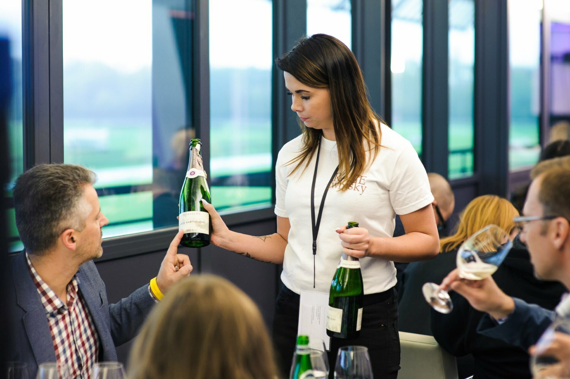 Girl in white shirt shows man at table the label on a bottle of wine