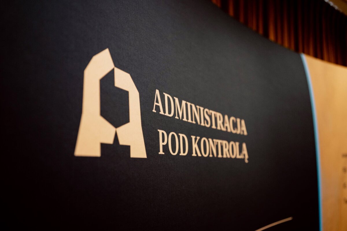 Baner z białym geometrycznym logo przypominającym literę „A” i polskim napisem „ADMINISTRACJA POD KONTROLĄ”, czyli „ADMINISTRACJA POD KONTROLĄ”. Na ciemnym tle po prawej stronie znajdują się częściowo widoczne zasłony. Jest to idealne rozwiązanie do fotorelacji z eventu, oferując efektowną oprawę wizualną dla Twojego kolejnego fotografa eventowego.