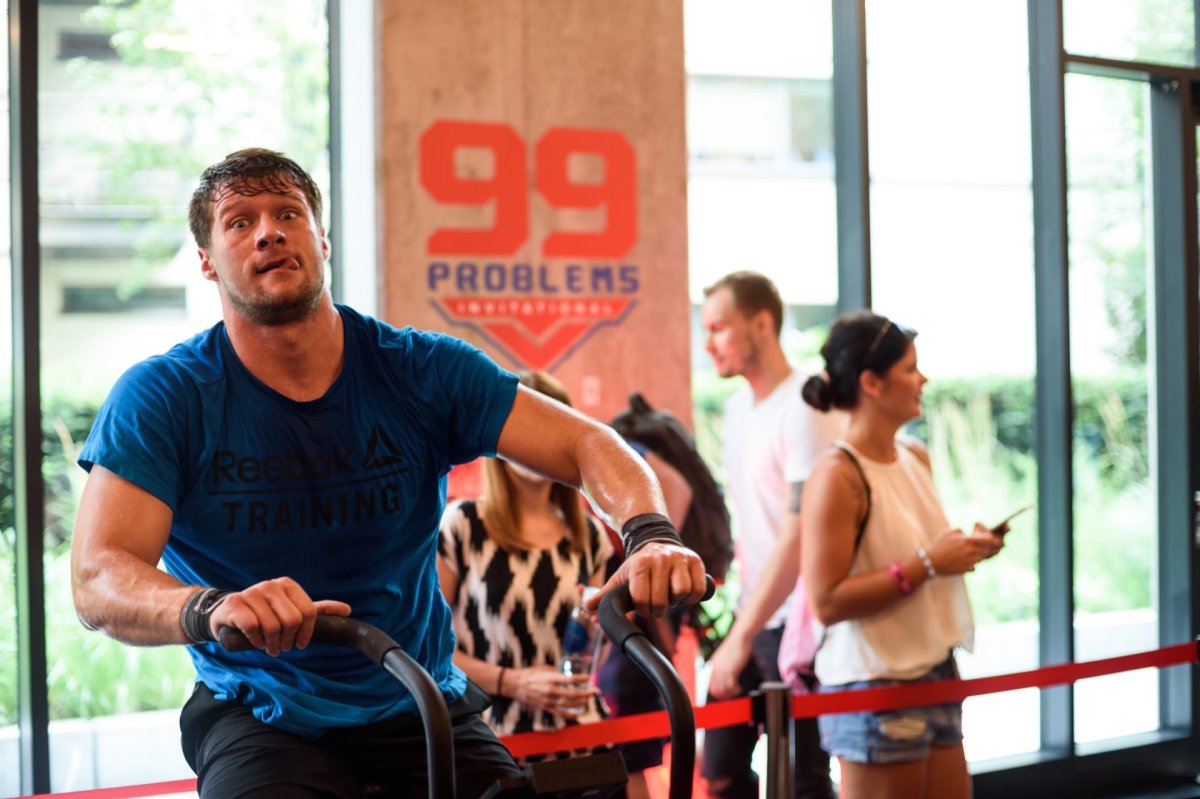 Man in blue reebok T-shirt on exercise bike shows tongue