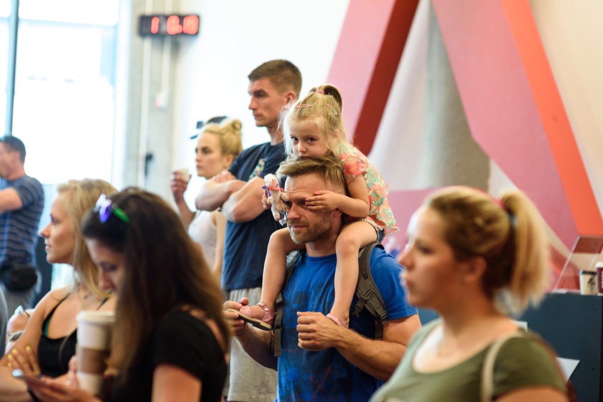 A girl in the audience sits on her dad's shoulders and looks into the lens