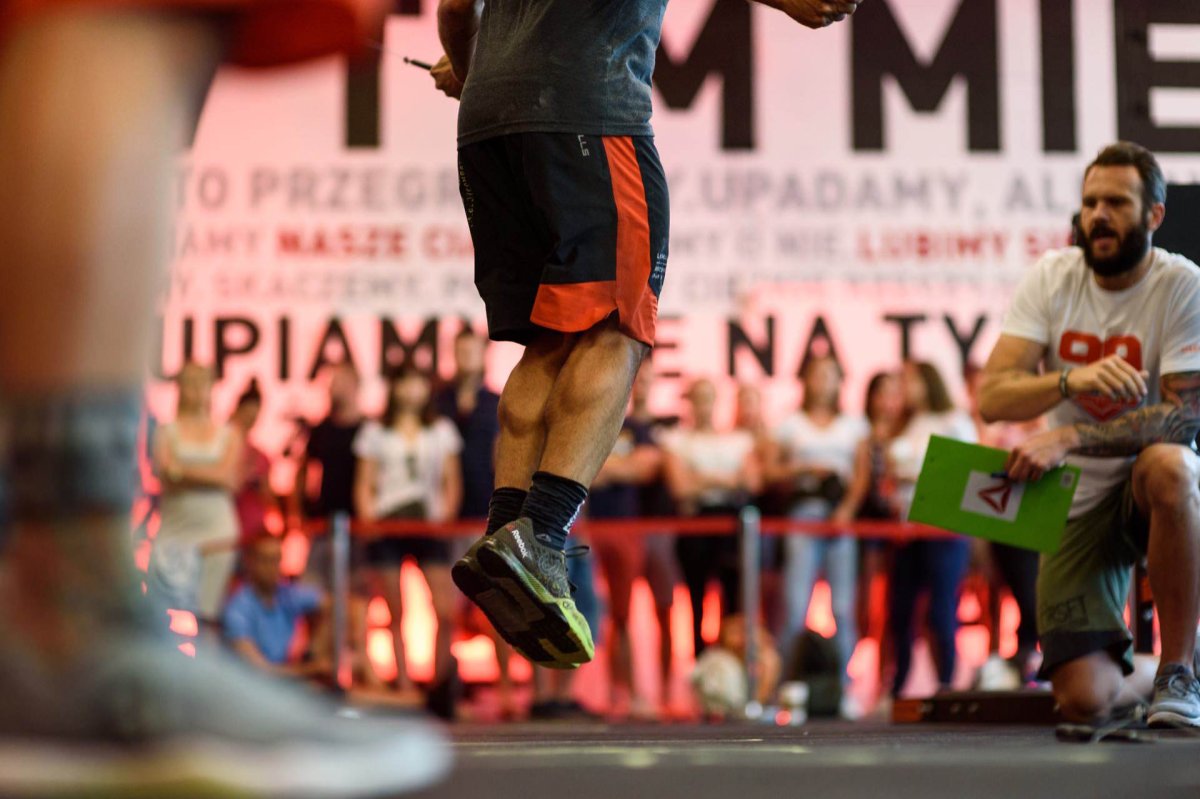 Muscular legs of a man who jumps on a skipping rope and in the background a judge counting the number of them