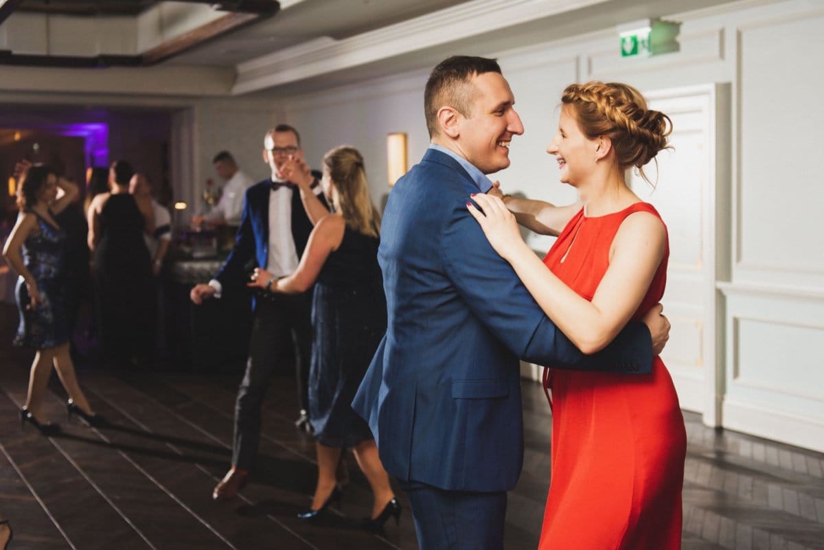 A woman in a red dress and a man in a navy blue suit dance and have fun on the dance floor