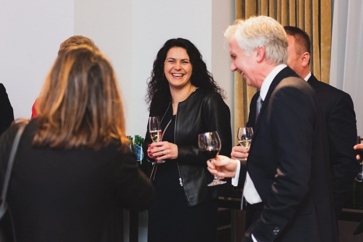 People with glasses of wine and champagne at a corporate event laugh to themselves