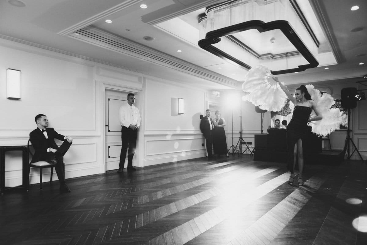 A woman with plumes dances for a man sitting on a chair