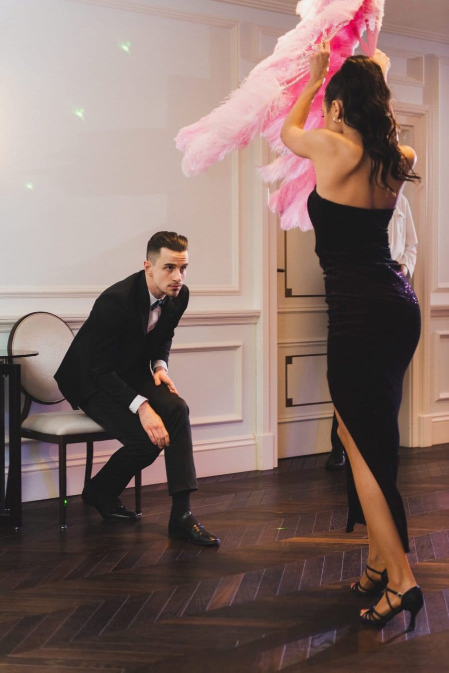 Woman with pink bureaus dances in front of a man on a chair