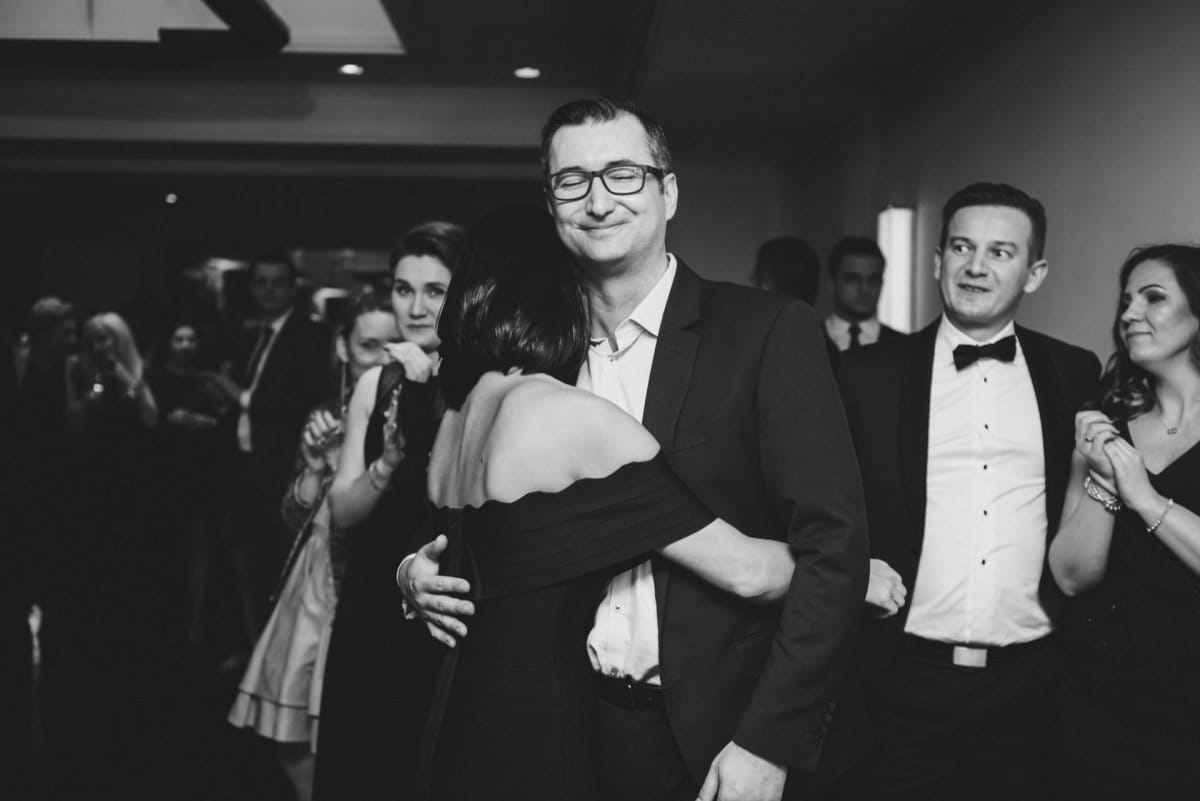 elegant man with glasses embraces woman in black dress