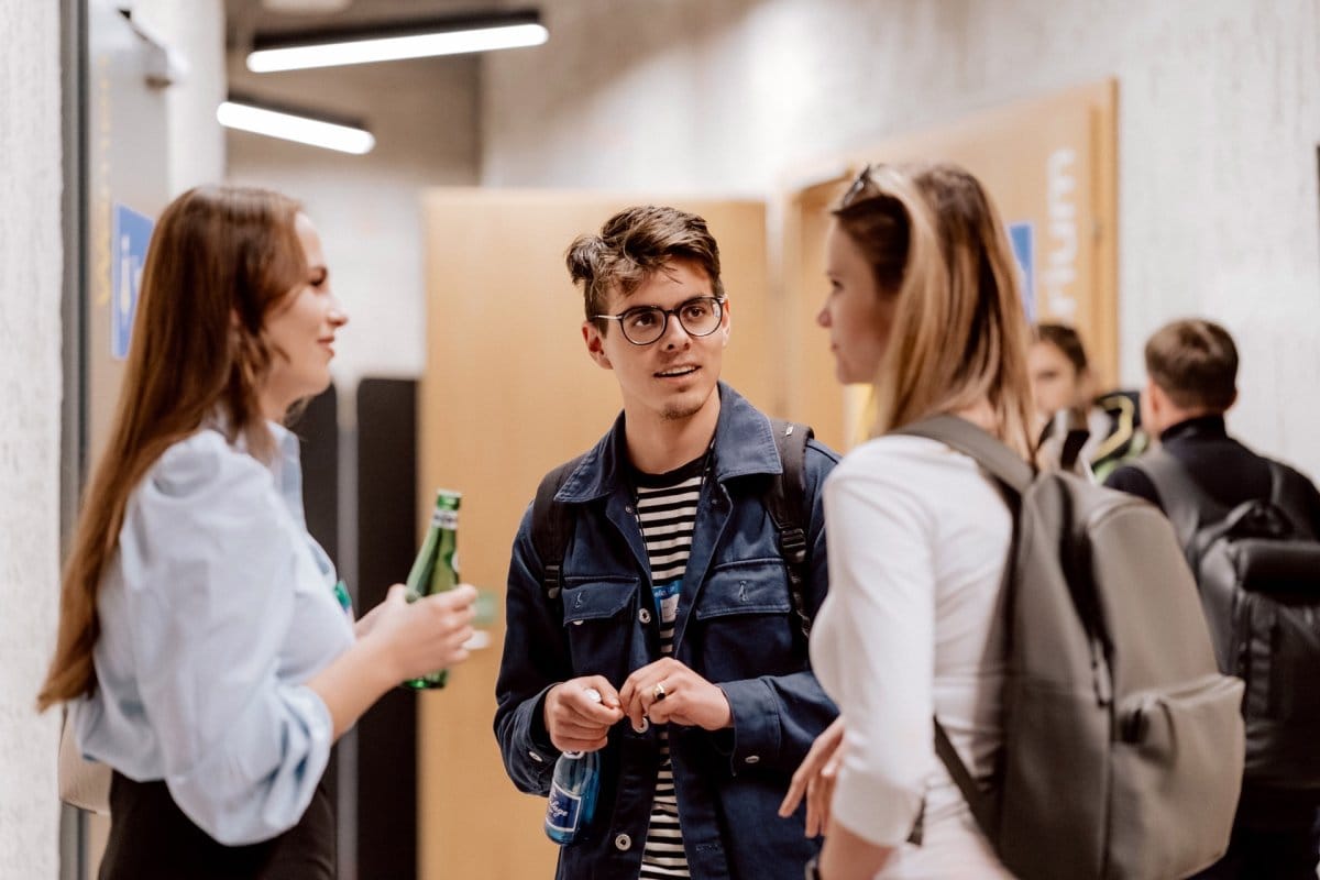 Two girls and a boy with glasses talk while drinking water