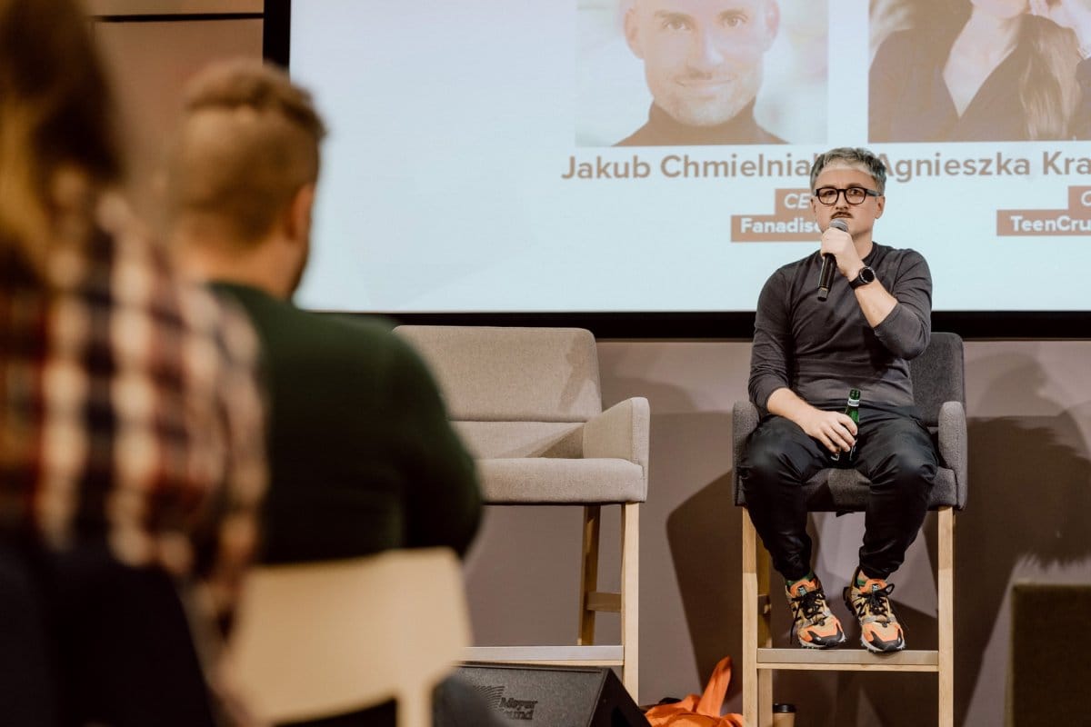 Artur Kurasinski speaks into the microphone while sitting on a high chair