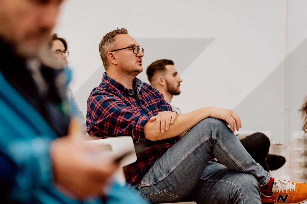 A conference attendee wearing a plaid shirt says toward the stage