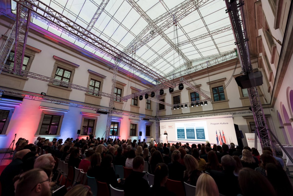 A large audience is seated in an open room with a high transparent ceiling. The presenter is on stage in front of a screen displaying a presentation with many slides. Modern interiors, colorful lighting and historic architectural elements created the setting for Marcin Krokowski's photo-reportage of events.  