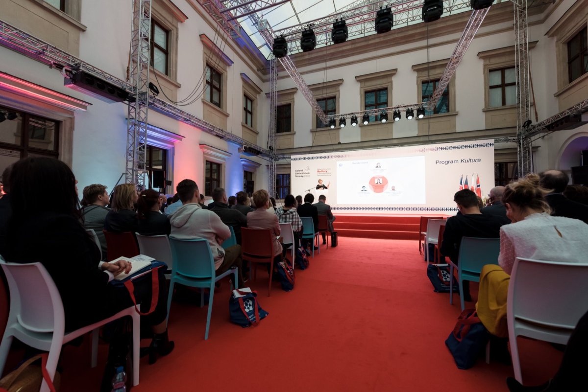 A group of people seated in rows attend the presentation in a spacious, well-lit room with a high ceiling and large windows. The presentation screen displays the words "Culture Program," and the experience is enhanced by professional lighting and audiovisual equipment, ideal for event photography. 