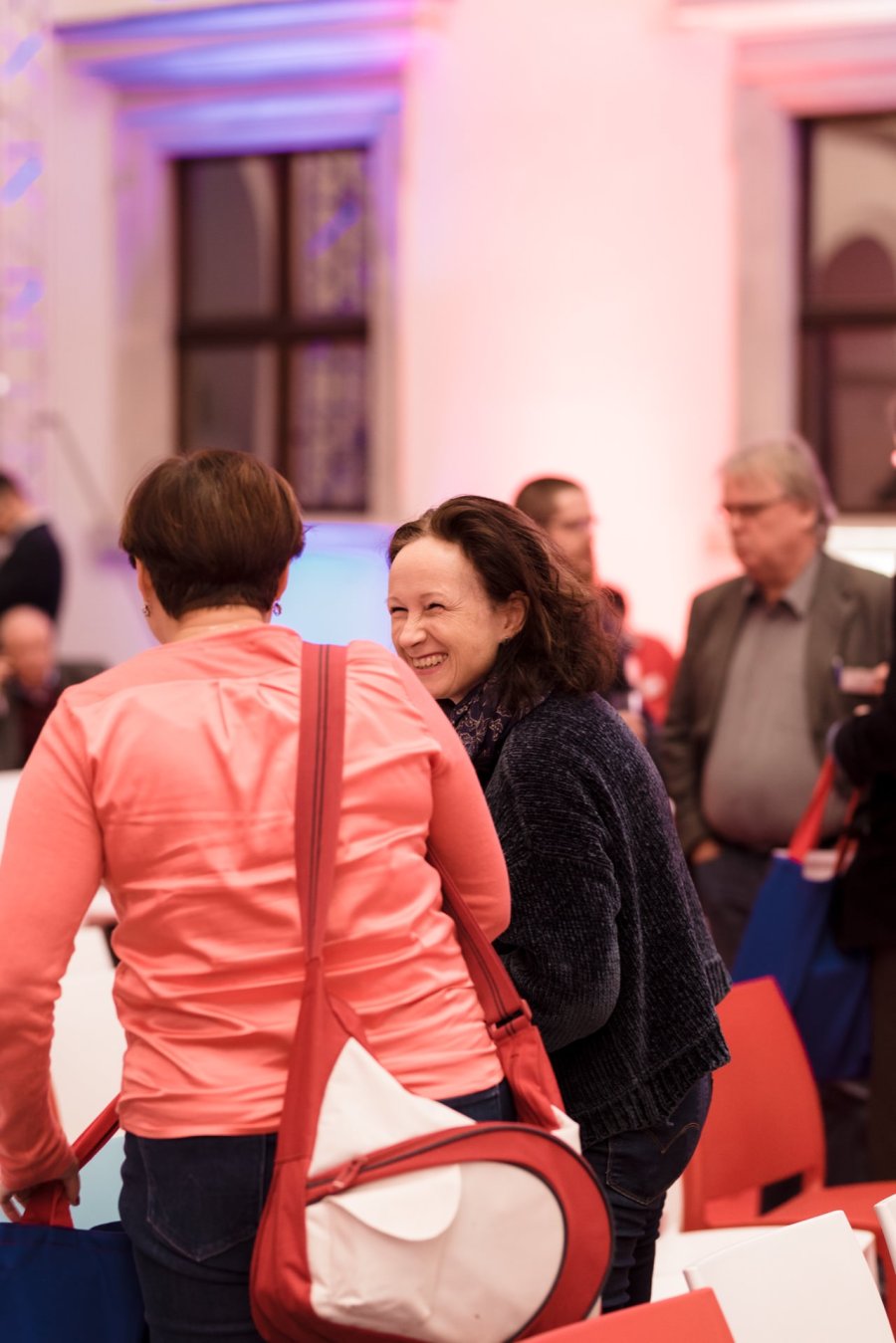 During the event, a group of people gather in the room. A woman with dark hair is smiling and talking to another woman who is holding a red and white bag. In the background, several other people can be seen interacting and talking to each other. This vibrant scene was captured by Marcin Krokowski, an established event photographer Warsaw.   