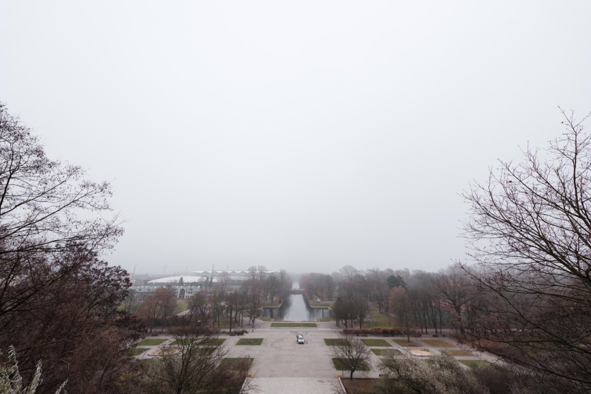 The hill overlooks a misty landscape with a view of a rectangular pond surrounded by leafless trees. In the foreground is a nearly empty parking lot with a single car. The background is shrouded in a thick fog, typical of event photography.  