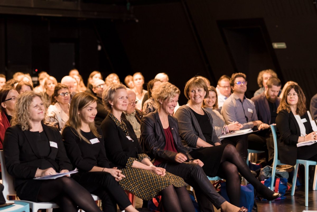 In the conference room, a group of people sit attentively in rows of chairs, facing forward. Most of the participants are dressed in business attire, and many are smiling or busy, with notepads or documents in their laps. Marcin Krokowski captures these moments beautifully as an event photographer in Warsaw.  