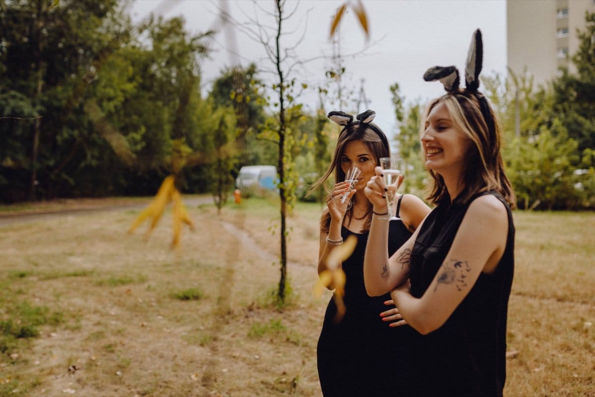 Girls in bunny ears drink champagne in park under block of flats