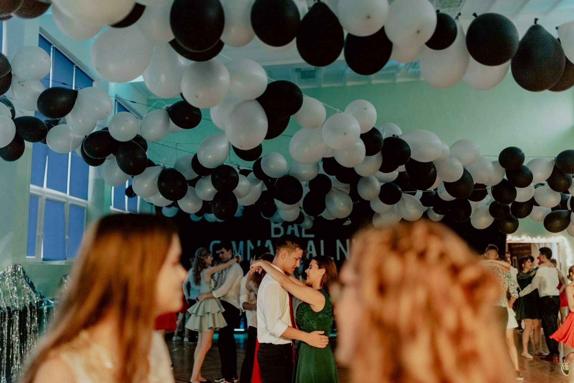 A group of people dancing in a decorated room with black and white balloons on the ceiling. Attention is focused on the dancing couple in the middle, while other guests are visible in the background. The atmosphere is festive, probably a party or dance event, perfect for those seeking the magic of event photography or hiring an event photographer Warsaw.  