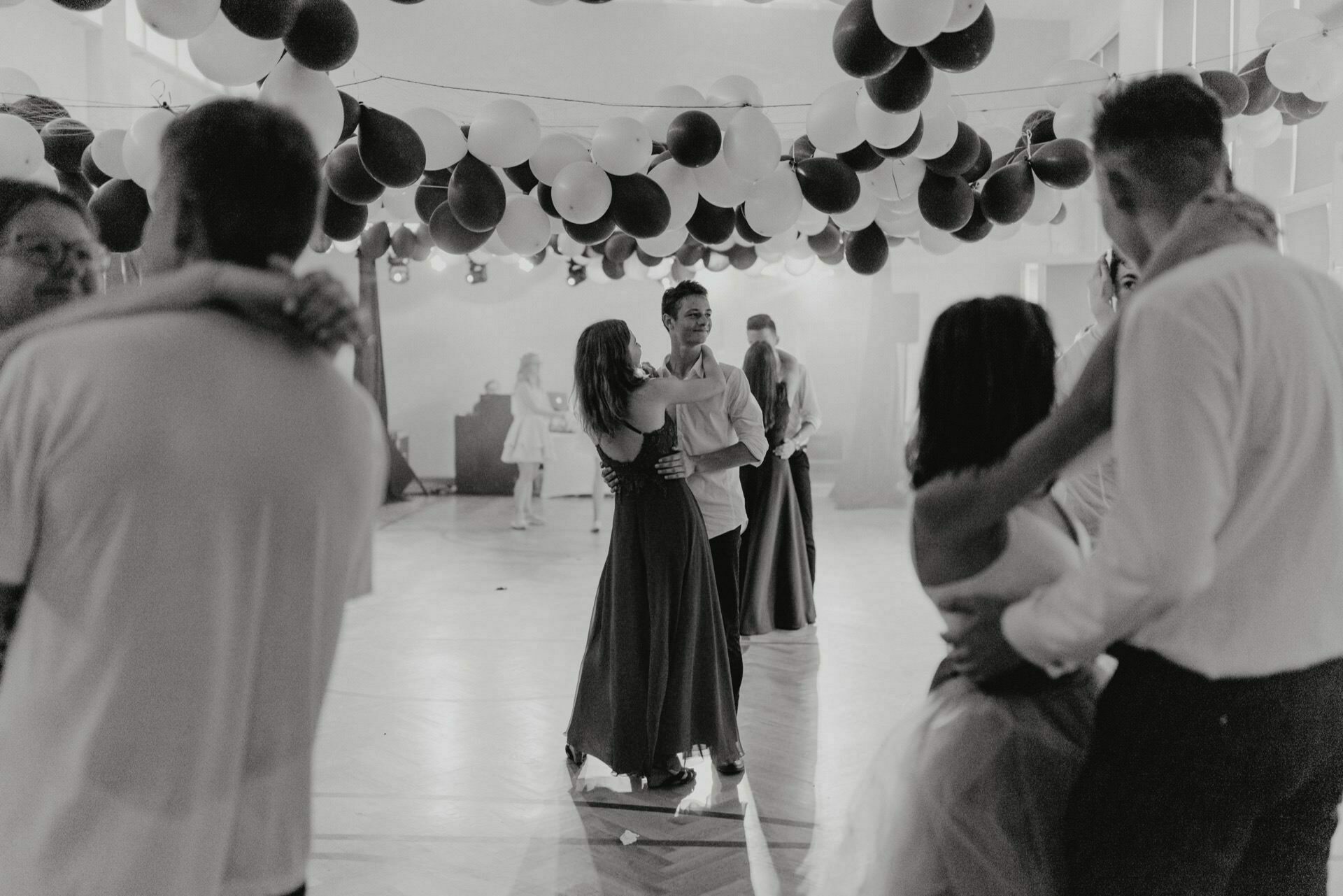 The black-and-white photo of the events shows couples dancing in a decorated room with balloons hanging from the ceiling. Three couples are visible: one in the middle and two on the sides, dressed in formal attire. The atmosphere seems festive and intimate, captured by a skilled event photographer Warsaw.  