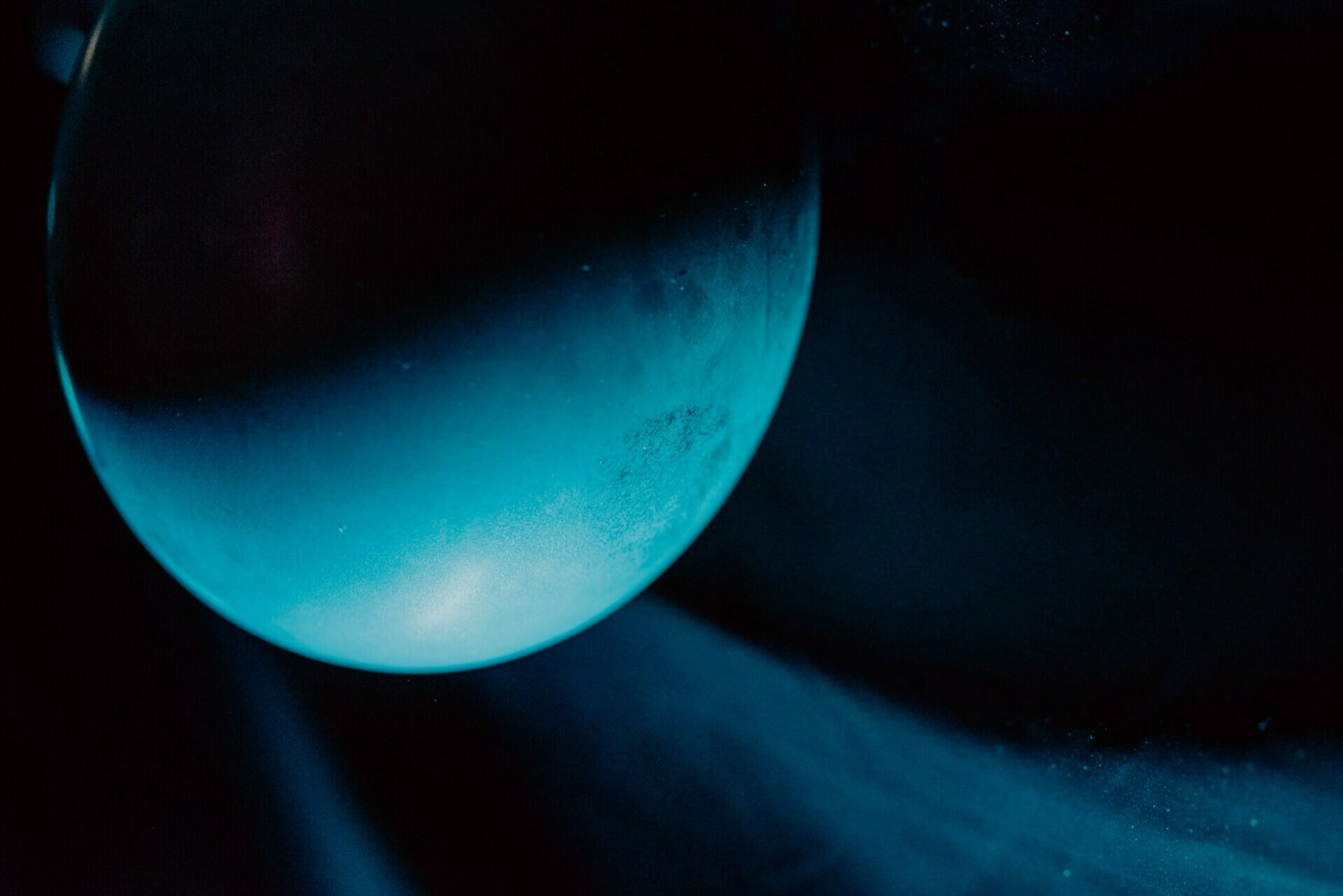 Close-up photo of a reflective glass sphere illuminated by blue light, set against a dark, almost black background. The light creates a gradient effect on the sphere, creating a mysterious and otherworldly atmosphere - the perfect element for any photography event. 