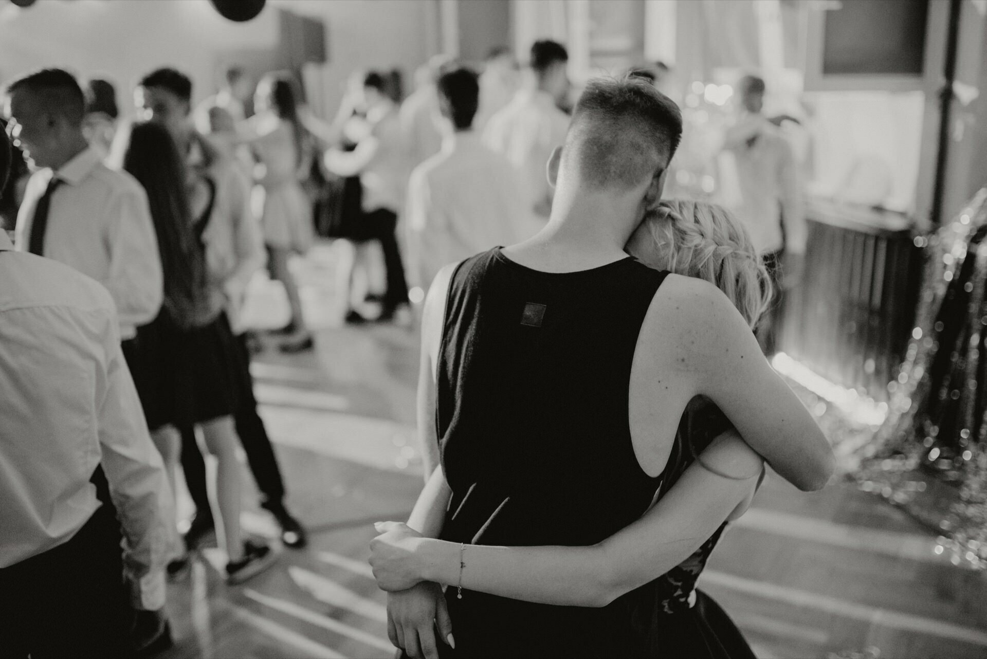 The black and white photo of a couple dancing at a crowded party or event captures the essence of event photography. They are facing away from the camera, holding a hand on the other person's shoulder. In the background, other guests are talking and dancing. The atmosphere is lively and festive, perfect for any event photo shoot.   