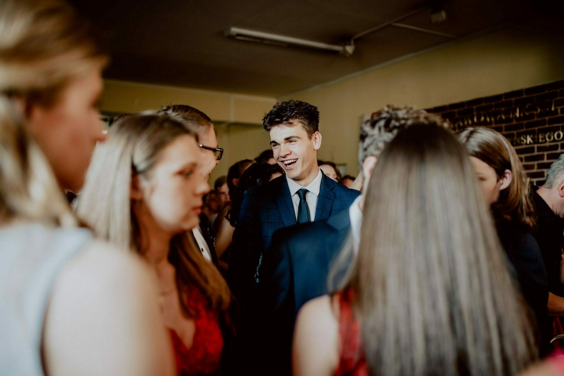 A man in a dark suit stands, smiling and chatting with a group of people at a social event. The background is softly lit and everyone is busy talking. Some are wearing formal attire, suggesting that this may be a meeting or celebration - an ideal location for event photography.  