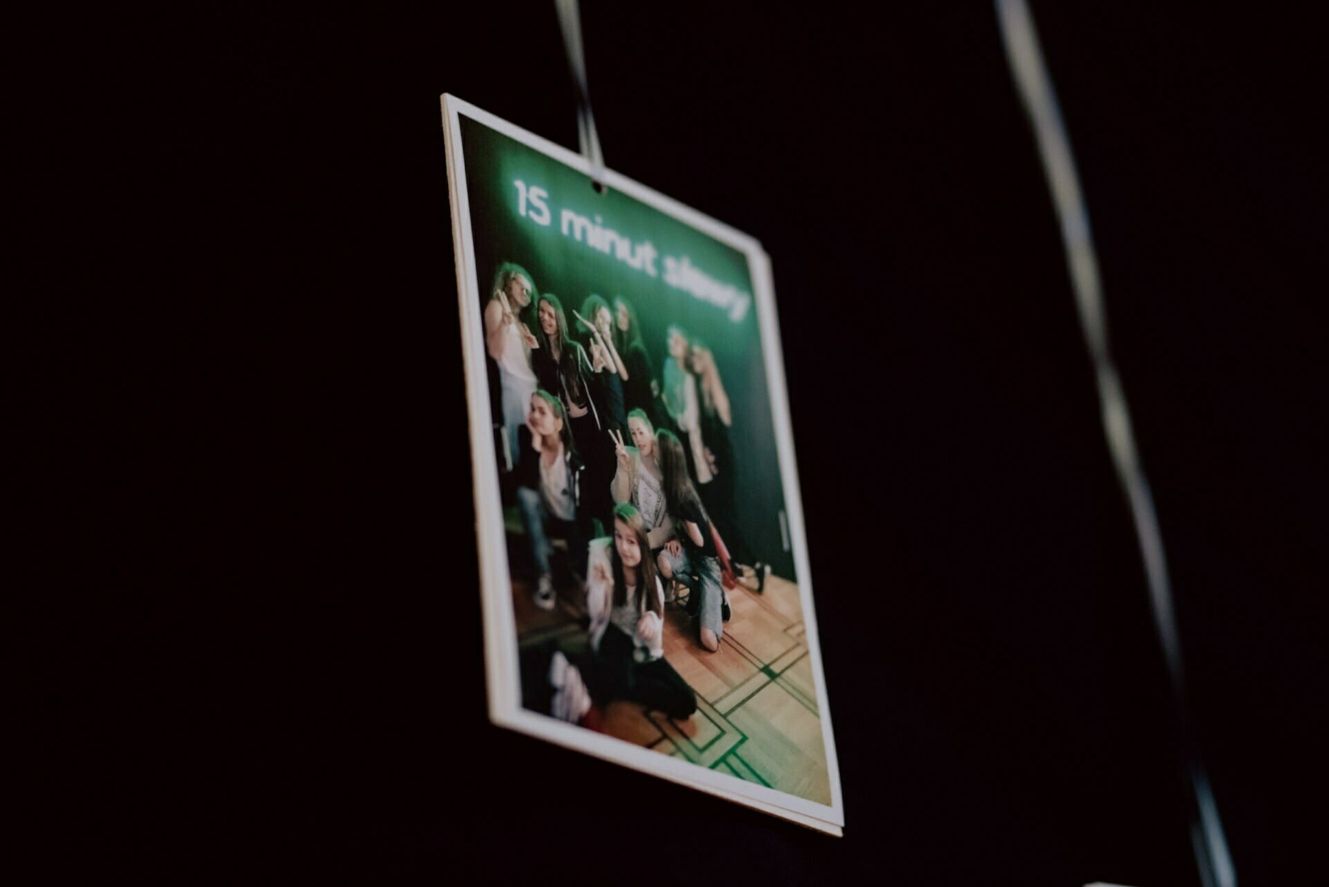 A vertical photo of a group of people posing together against a green background, perfect for capturing moments in event photography. The top part of the image contains smudged white text, which probably reads "15 minutes of slávy." The background is dark, highlighting the brightly lit photo.  