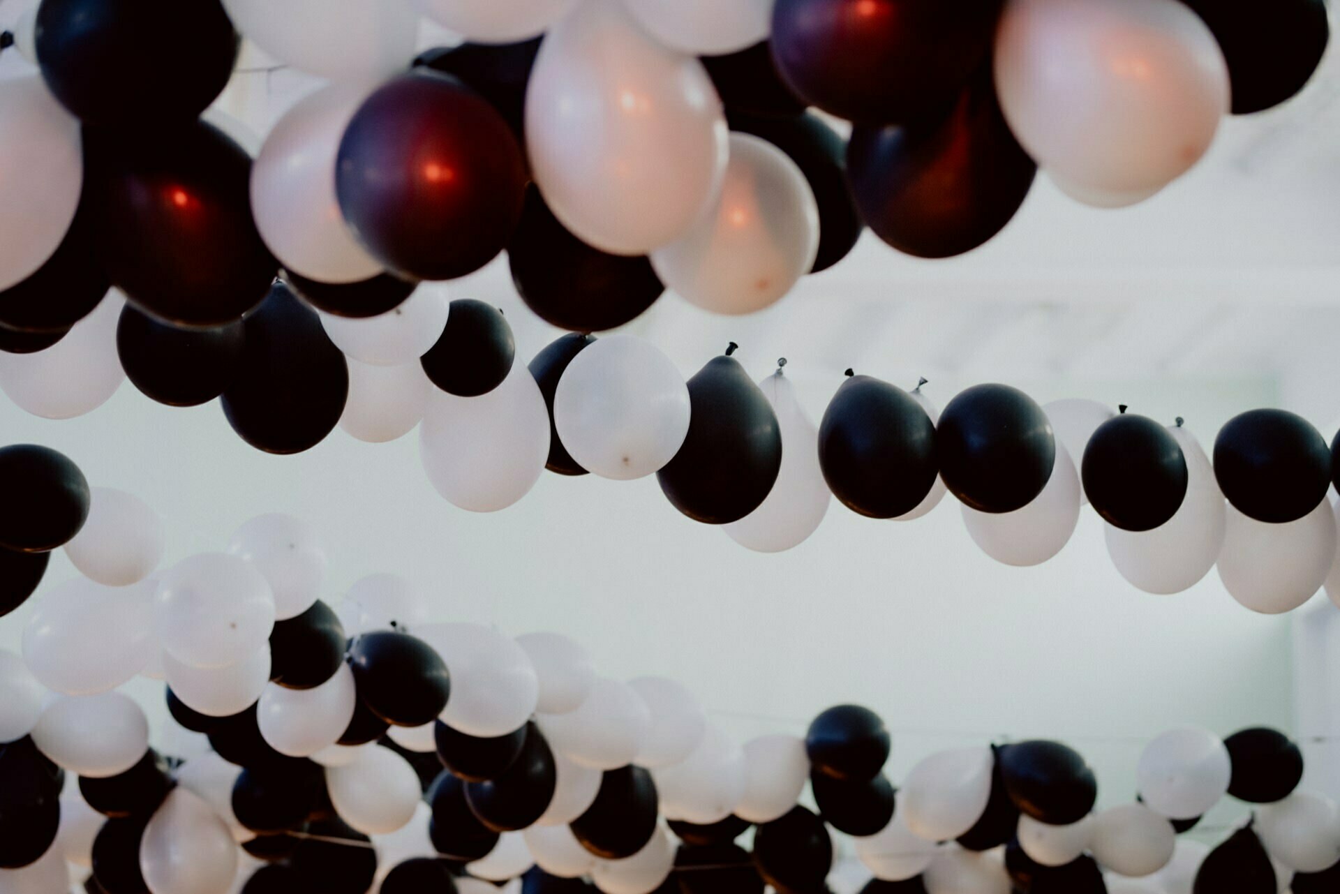 The ceiling is decorated with numerous black and white balloons, evenly arranged in alternating colors, creating a festive and elegant atmosphere. This event photo captures the depth of the decor in perspective, showing the intricate details of this event photography. 