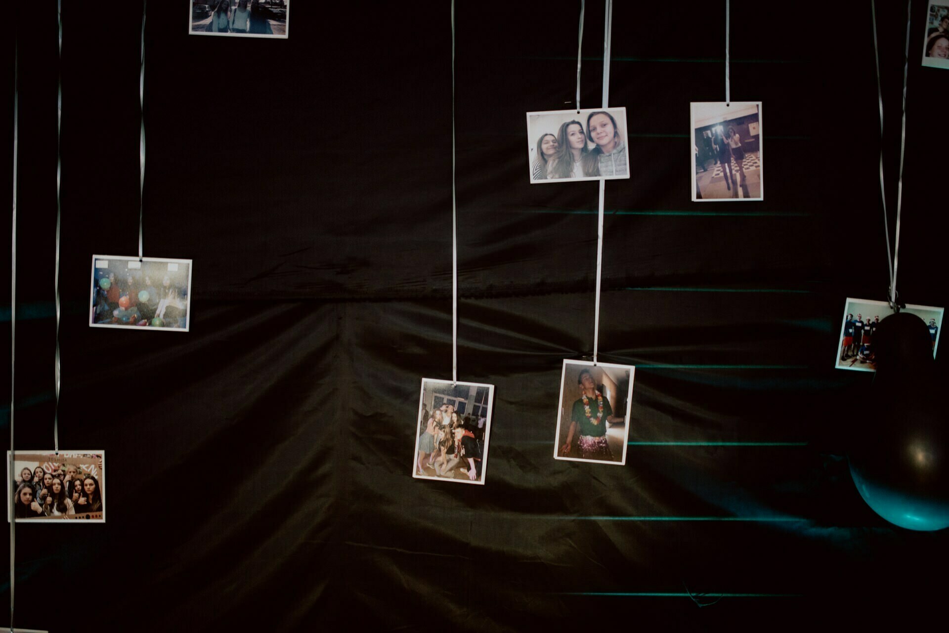 Polaroid photos hanging on strings against a dark background capture vivid moments by an event photographer warsaw. Groups of people smile and pose in each photo, which hangs at different heights for a shifted effect. On the right side of the photo, a balloon is partially visible, completing the lively event photography.  