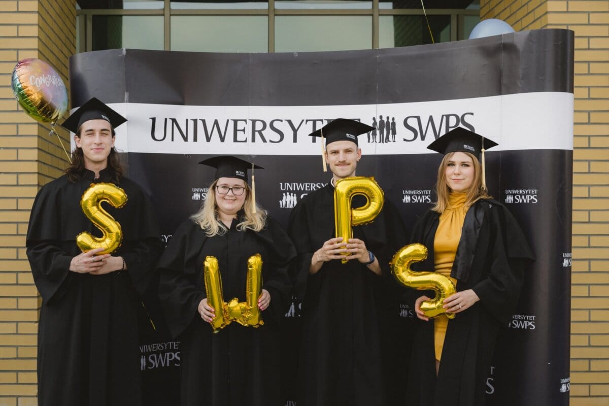 Four graduates stand in front of a banner reading "SWPS University." They are wearing black graduation gowns and caps, holding gold balloons with the letters "SWPS" in their hands. A congratulatory balloon is visible on the left. This unforgettable moment was captured by Marcin Krokowski with a detailed photo report of the events.   