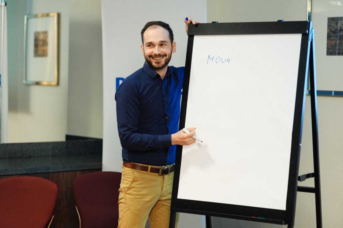 A man writing something down on a blackboard smiles at his listeners