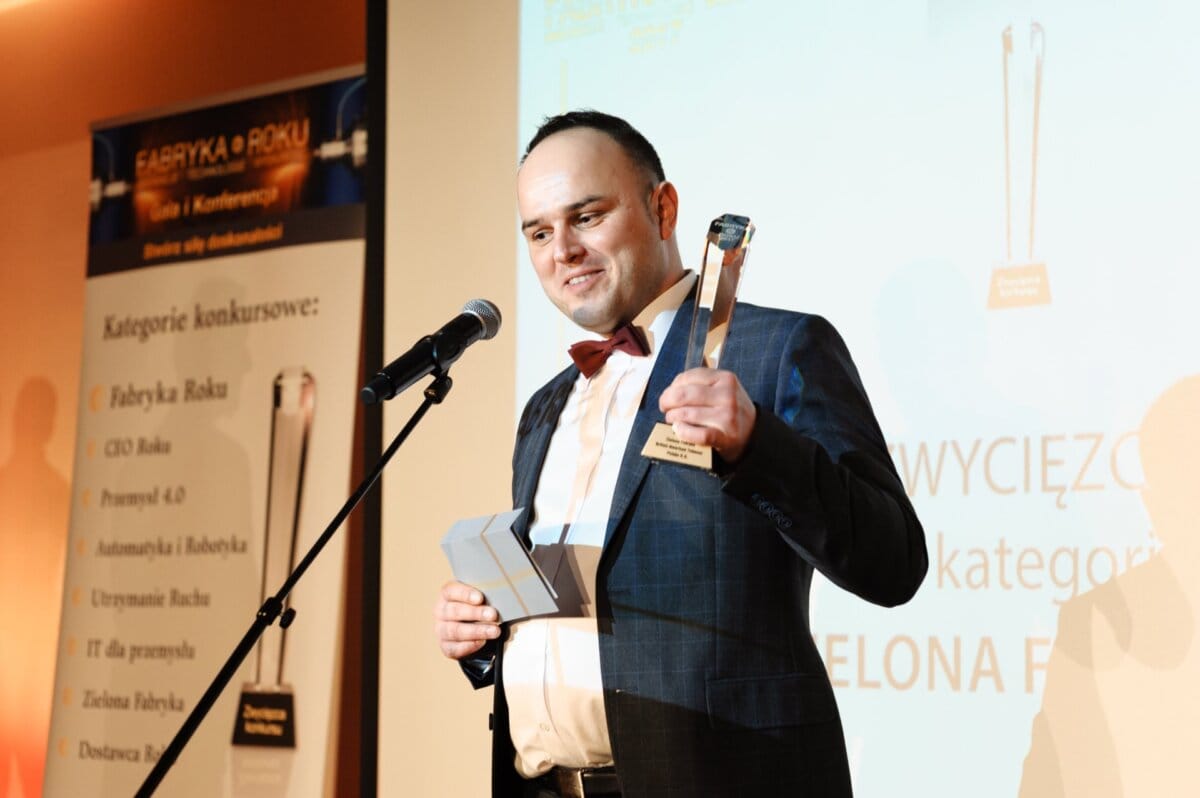 A man with a glass statuette in his hand speaks into a microphone on stage