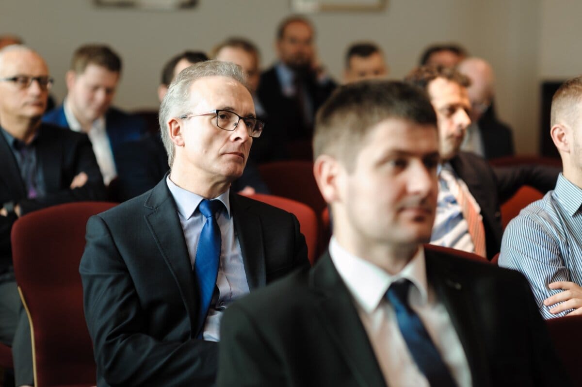 An elderly man dressed elegantly watches a presentation at a conference