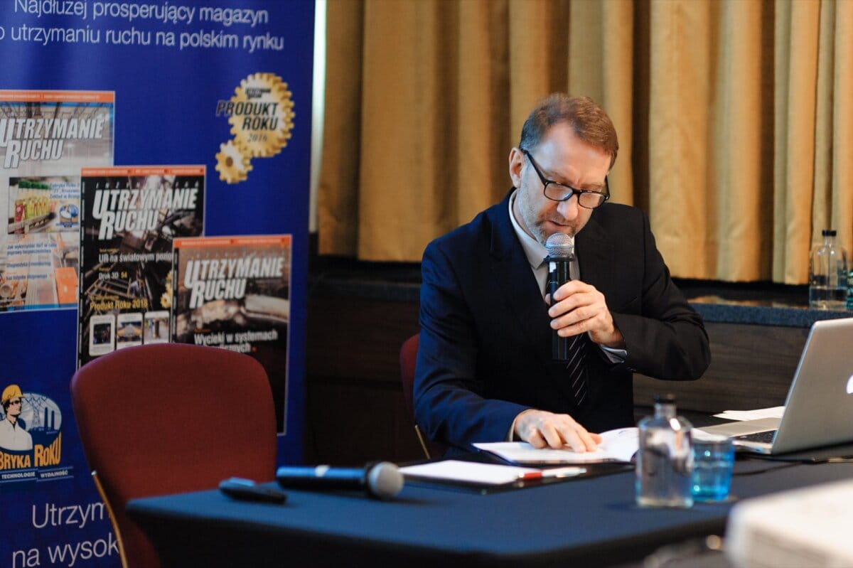 Man with glasses speaks into microphone while sitting at black table