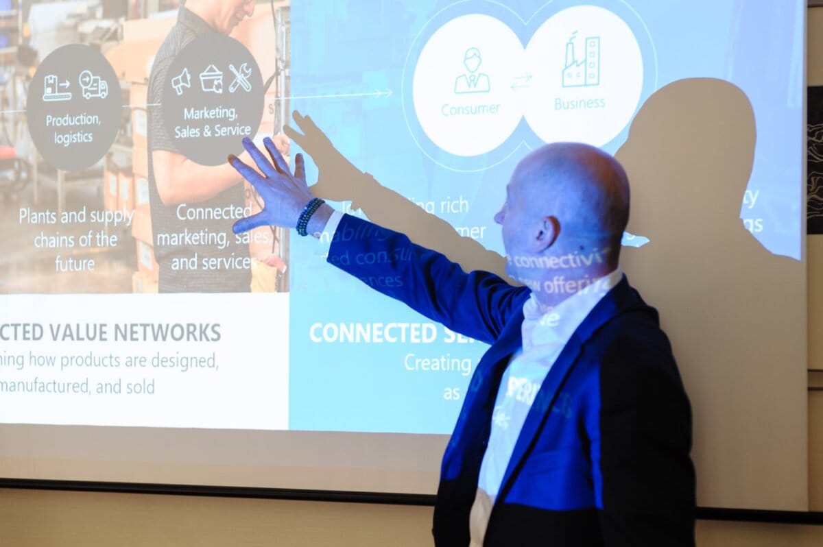 Man illuminated by light from overhead projector points to something on presentation