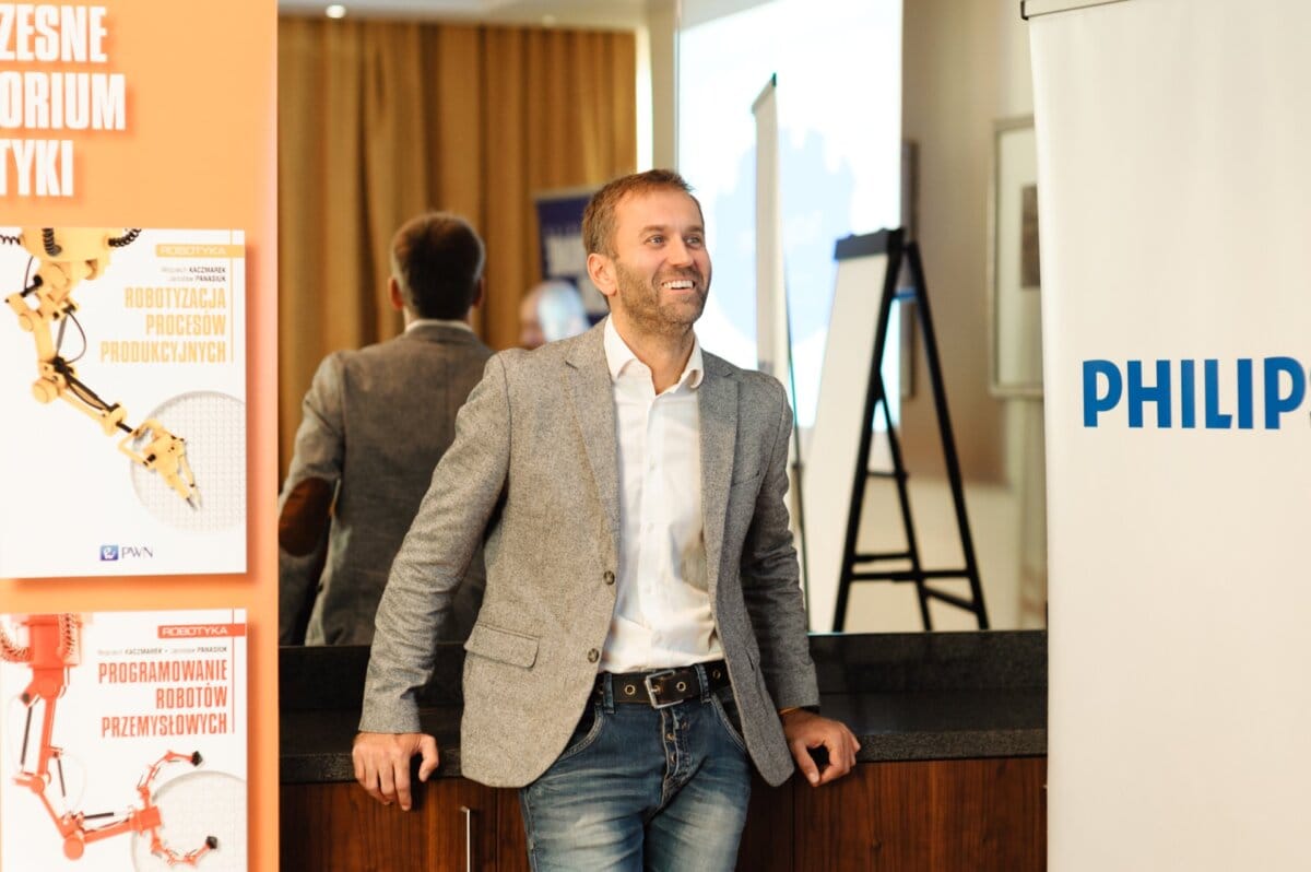 A man in a gray jacket smiles while leaning against a wall