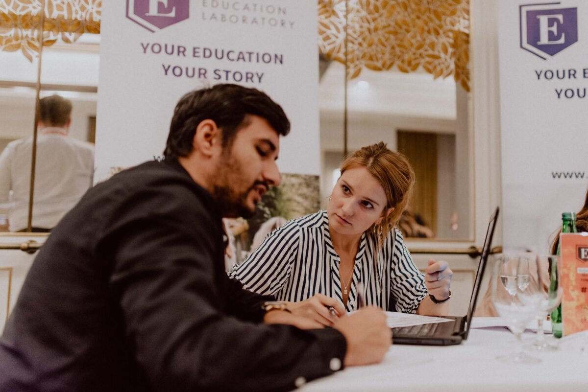 A man and a woman sit at a table in a professional setting and talk about something serious while looking at a laptop. They are part of the event, as can be seen from the banners with the words "Learning Lab" and "Your Education, Your Story" in the background. This photo report of the events perfectly captures the intensity of their discussions.  