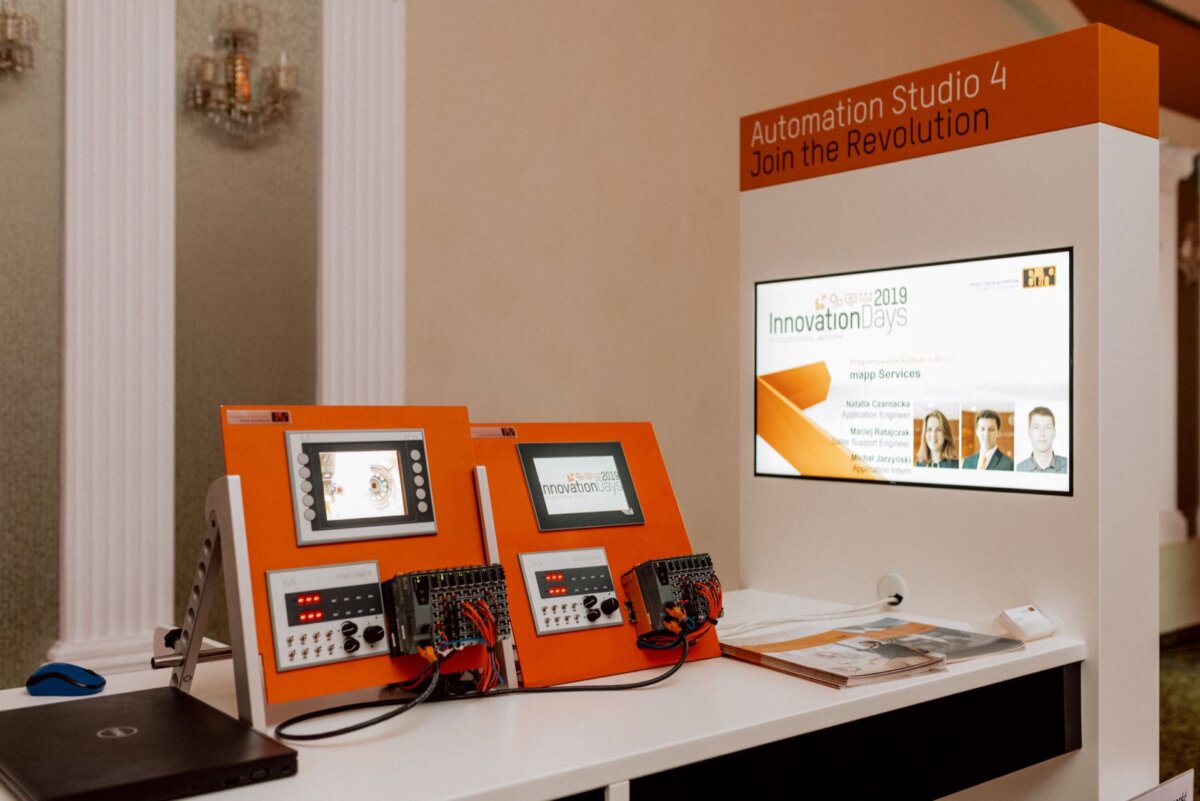 The exhibition booth showcased Automation Studio 4 with two interactive devices equipped with screens and control panels. In the background, a monitor with the words "Innovation Days 2019" and a banner with the text "Join the revolution" above the booth, all beautifully captured in an elegant interior setting by event photographer warszawa. 