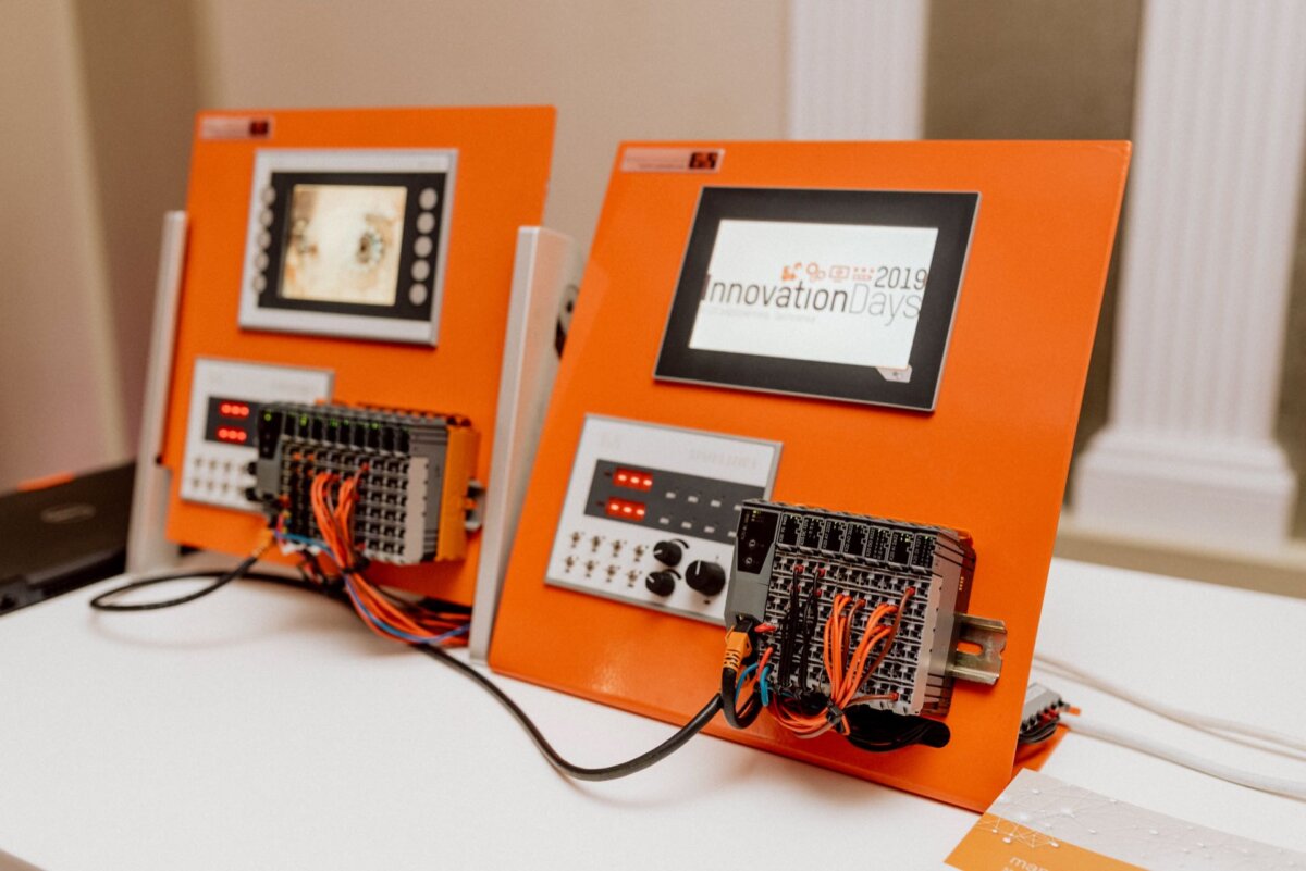 Two orange panels are displayed on a white table, equipped with small screens and circuit boards decorated with numerous wires. One screen bears the words "Innovation Days 2019." Both configurations appear to be used for technical or electronic demonstrations, beautifully captured as part of the event photography collection.  