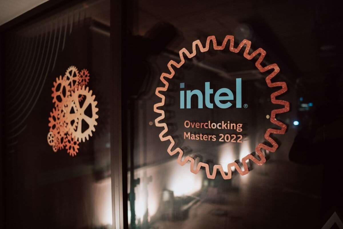 A glass panel with decorations of two gears and the words "Intel Overclocking Masters 2022" inside a large gear structure. The background is blurred and the ambient light creates a warm and inviting atmosphere, beautifully captured by the skills of event photographer Marcin Krokowski. 